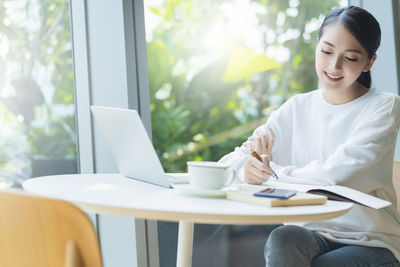 Young woman using phone while sitting on table