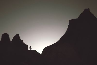 Low angle view of silhouette man standing on rock against sky