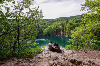 People sitting by lake against trees in forest