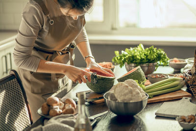 Kitchen scene with person preparing food, surrounded by fresh produce, cooking with care and passion