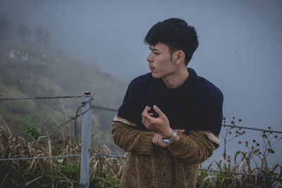Young man standing on mountain peak during foggy weather