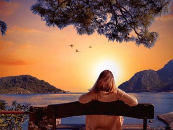 Rear view of woman looking at sea against sky during sunset