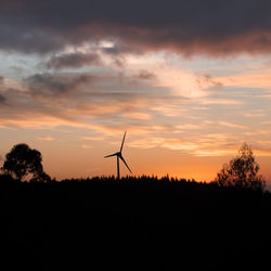 Silhouette of wind turbines on field against sky during sunset