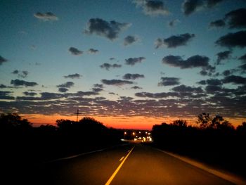 Road amidst silhouette trees against dramatic sky