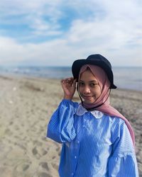 A girl is standing on the beach with the sea, waves and sky in the background