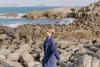 Woman standing on rocky shore against sky