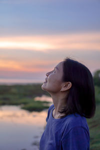 Woman looking up while standing against sky during sunset