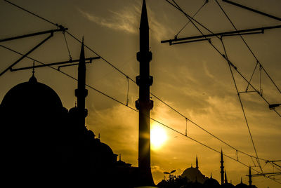 Low angle view of silhouette electricity pylon and mosques against sky during sunset in istanbul