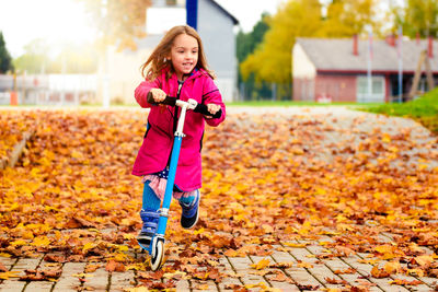 Portrait of girl riding push scooter at park during autumn