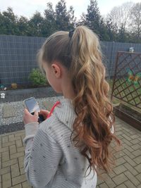 Woman holding mobile phone while standing on fence