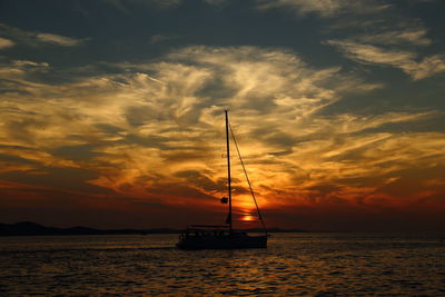 Silhouette sailboat in sea against sky during sunset