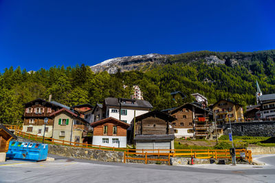 Houses by road against buildings and mountains against clear blue sky