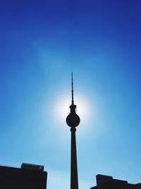 Low angle view of communications tower in city against blue sky