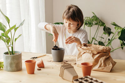 A cute little girl is transplanting a home flower at home. pour soil into the pot.