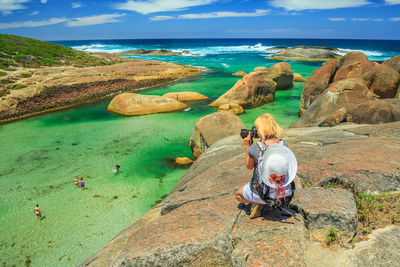 Woman sitting on rock by sea against sky