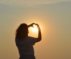 Rear view of woman standing against sky during sunset