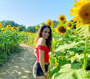 Portrait of smiling woman standing by sunflower on field