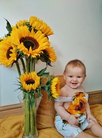 Full length of cute girl holding sunflower against yellow flowering plant
