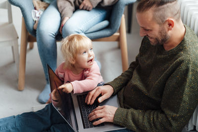 Daughter pointing at laptop on father's lap with mother in background