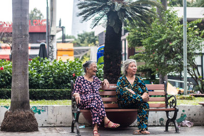 Woman sitting on bench against trees