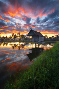 Built structure by lake against sky during sunset