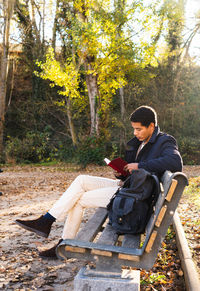 Full length of man reading book sitting at bench at park