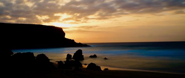 Silhouette rocks on beach against sky during sunset