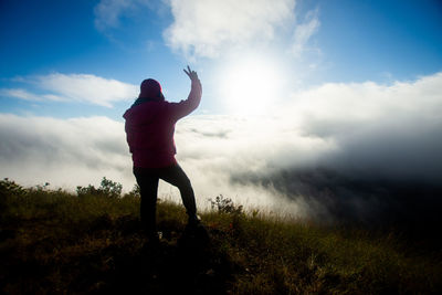 Rear view of woman with arms raised gesturing peace sign while standing on field against sky