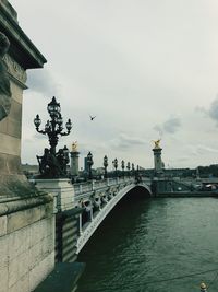 Statue of bridge over river against cloudy sky