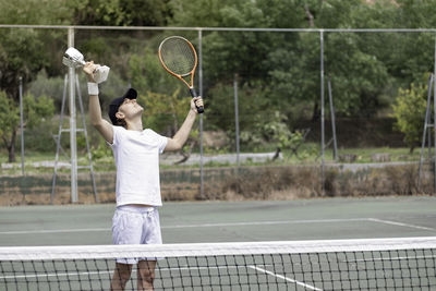 Professional man tennis player enjoying victory with cup in hand. looking up at sky and raising arms