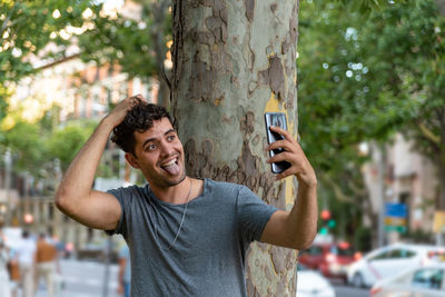 Portrait of young man using mobile phone against tree trunk