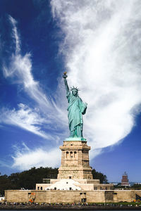 The statue of liberty and liberty island full of tourists on sunny day with white clouds blue sky