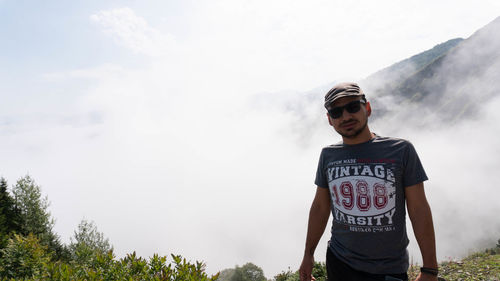 Young man wearing sunglasses standing against sky