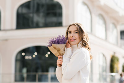 Young caucasian woman holds a purple bouquet of flowers in her hands and walks along a city street