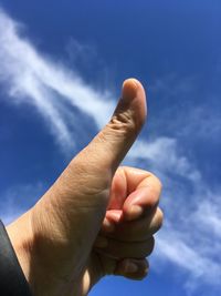 Close-up of cropped hand showing thumbs up against blue sky