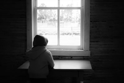Rear view of woman looking through window at home
