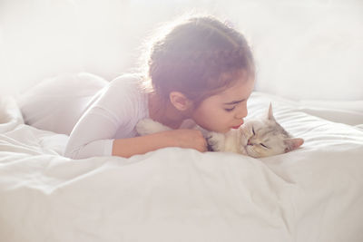 Portrait of a beautiful little girl, lies on a clean, white bed with a white british cat.