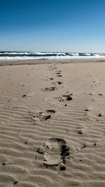 Footprints on sand at beach against clear sky