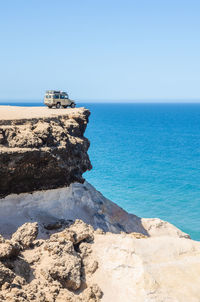 Land vehicle on cliff by sea against sky