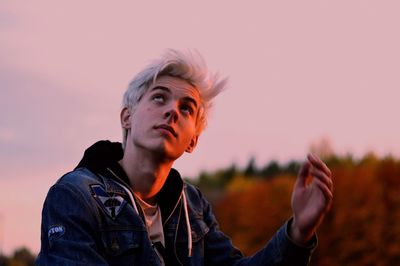 Portrait of young man looking away against sky during sunset