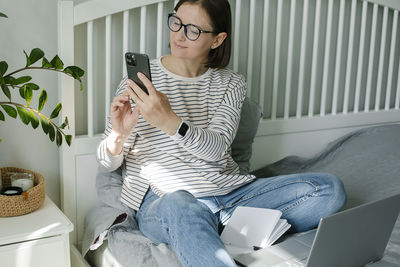 Young woman using mobile phone while sitting on sofa at home