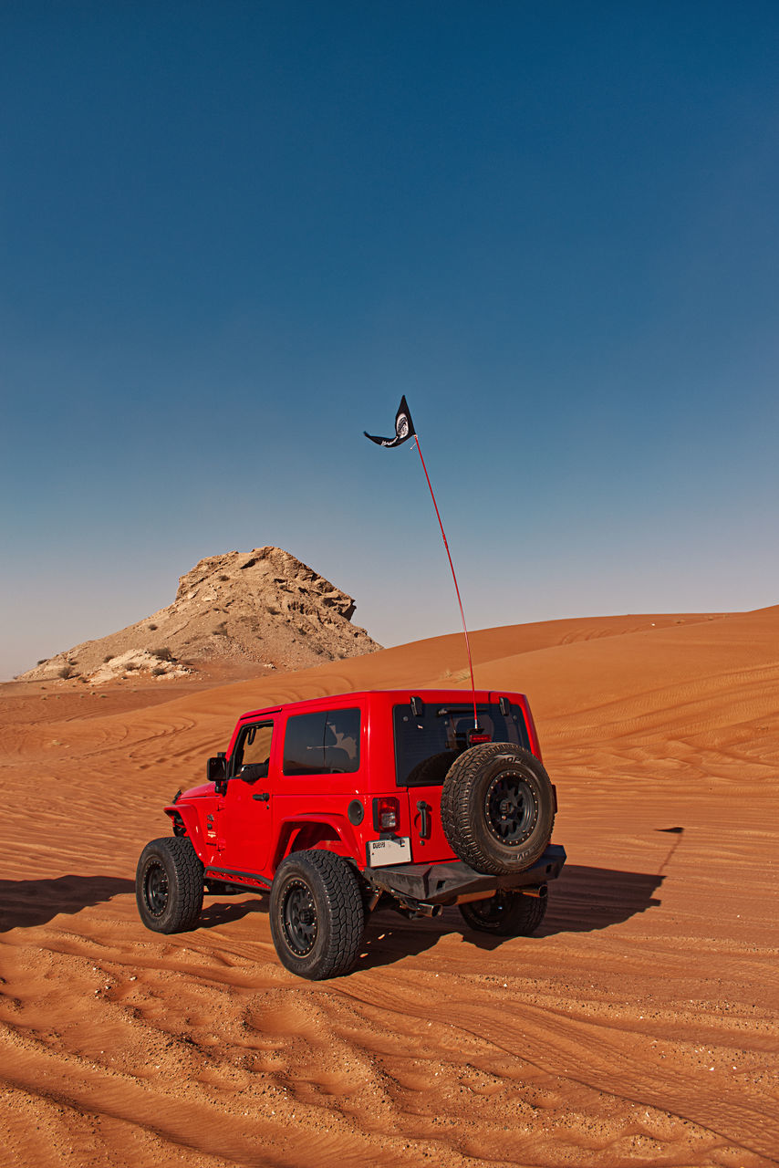 natural environment, desert, landscape, transportation, land, mode of transportation, erg, sky, nature, environment, sand, blue, scenics - nature, travel, clear sky, land vehicle, motor vehicle, sand dune, climate, arid climate, vehicle, copy space, sunny, car, day, sunlight, red, no people, off-roading, adventure, remote, outdoors, beauty in nature, horizon over land, off-road vehicle