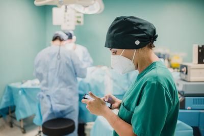 Female nurse using mobile phone inside operation room at modern hospital - focus on woman face