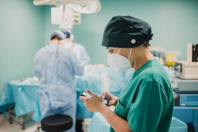 Female nurse using mobile phone inside operation room at modern hospital - focus on woman face