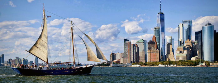 Sailboats sailing on sea by buildings against sky in city