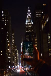 Cropped image of hand photographing chrysler building in city at night