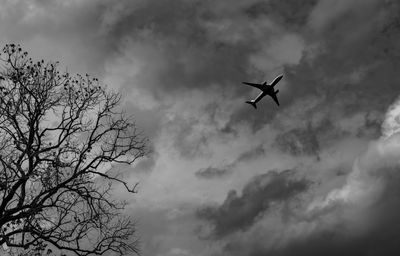 Low angle view of silhouette airplane against cloudy sky