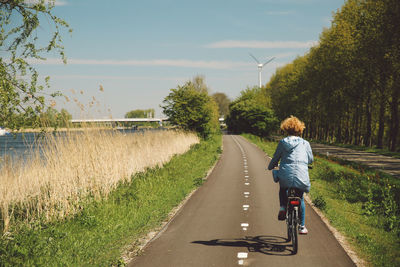 Rear view of woman riding bicycle on road by river