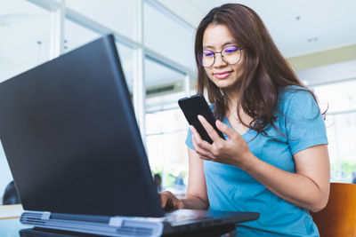 Young woman using mobile phone while sitting in laptop