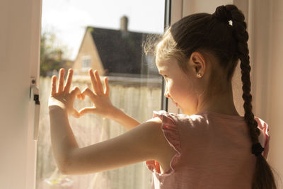 Rear view of girl looking through window at home